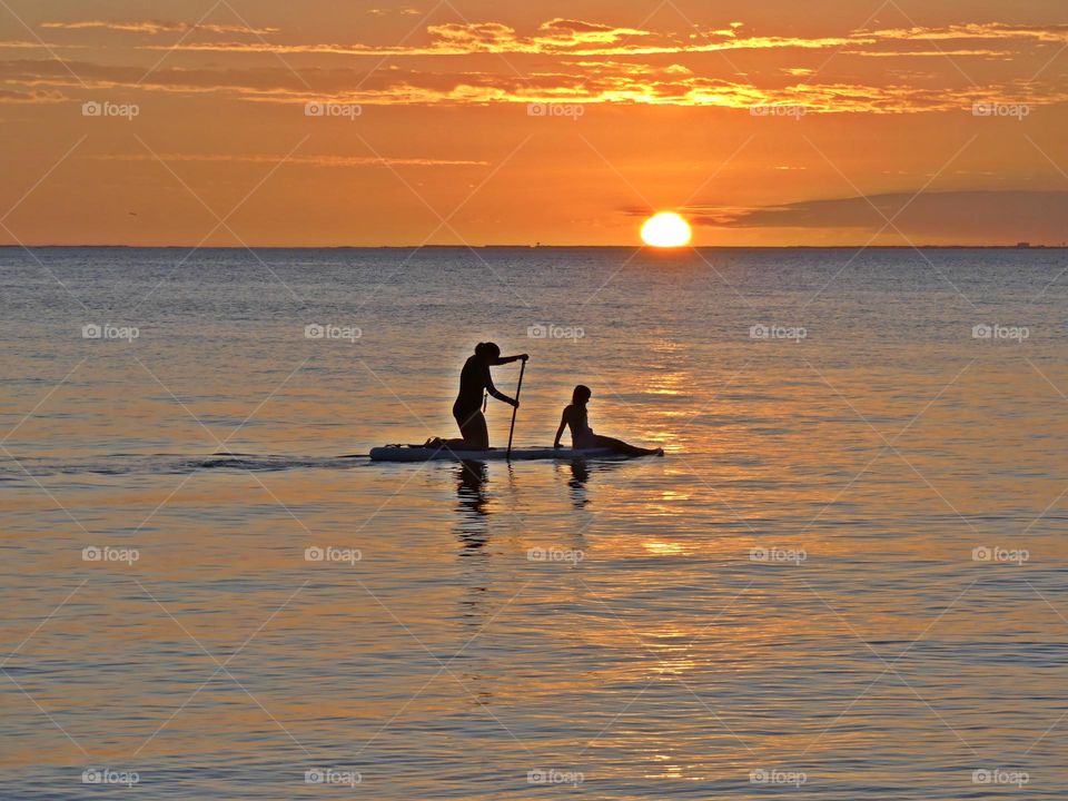 Magic Sunrises and Sunsets - Two surfer boarders paddle across the bay as the sunset as the descending orange ball slowly slips beneath the horizon