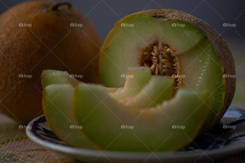 Slices of melon, half of melon and another melon in the background 