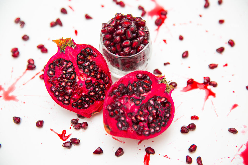 Healthy fresh pomegranates sliced with pips and seeds in a glass and scattered. Splashes of pomegranate juice. Fresh summer fruit for a healthy lifestyle on a white background.