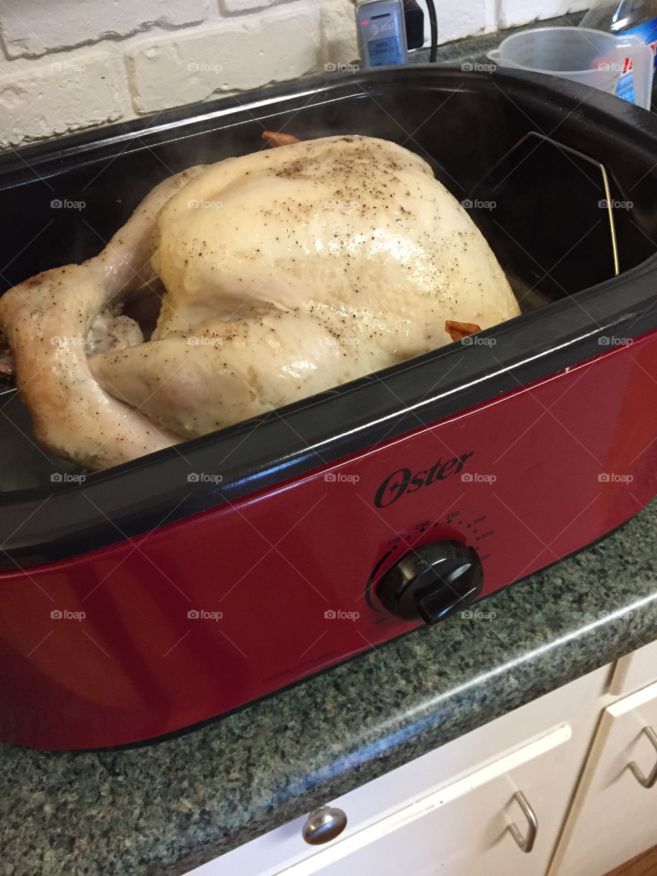 A turkey cooking for thanksgiving in a red cooker on the countertop.