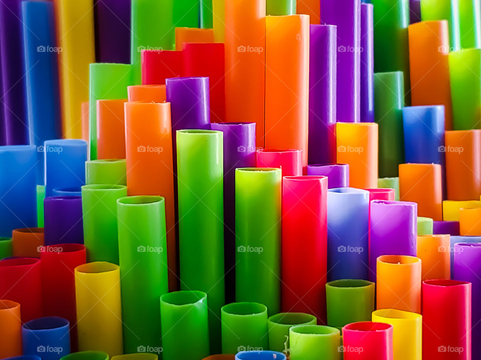 Rainbow colored plastic straws in a vertical position at various heights creating an interesting fun bright and colorful design subtly illuminated by natural morning light.