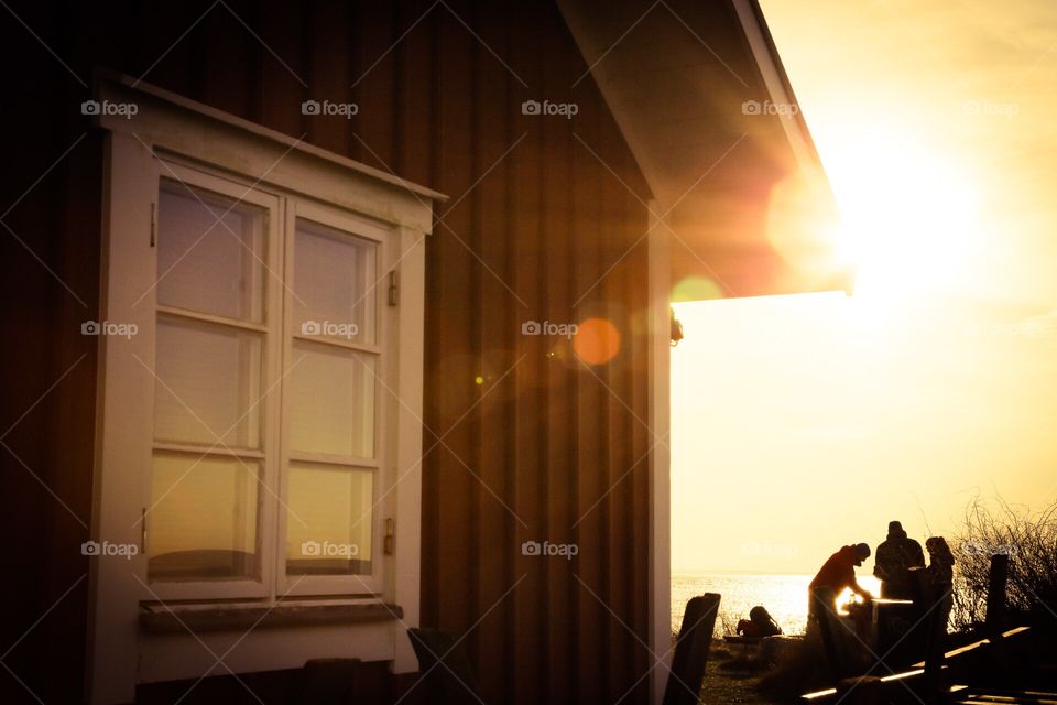 People together outdoors in the sunshine in winter by the red wooden house 