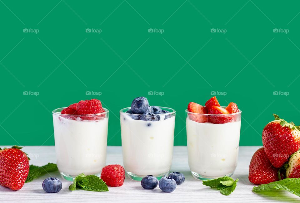 Mini yoghurt pots with colourful berries against a green background.