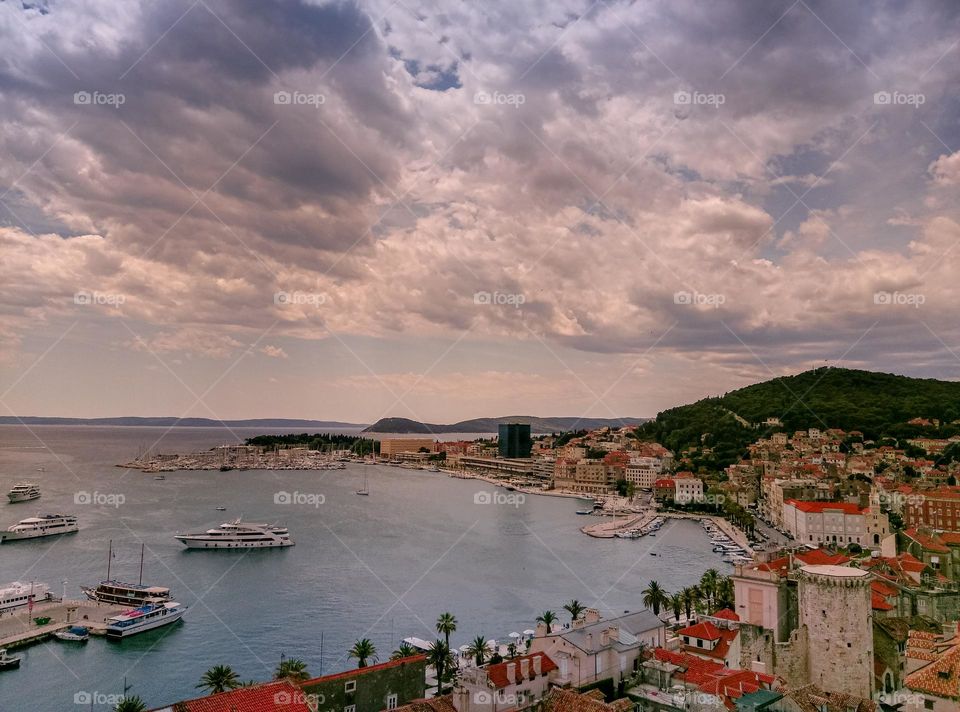 A bird's eye view over the city of Split, which is dotted with clouds above it and bathed in the beautiful Adriatic sea