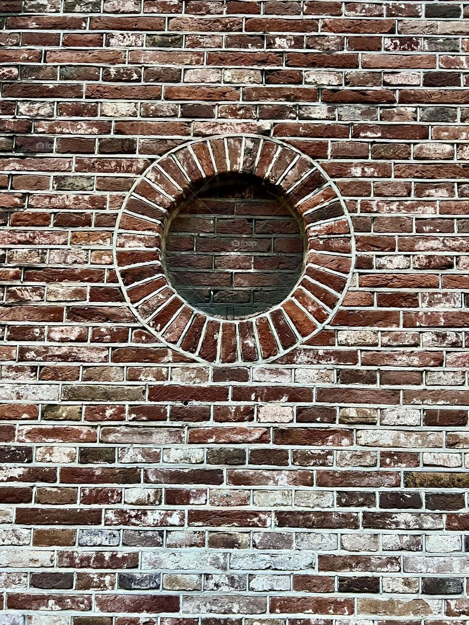 A round decorative element in a brick wall, made of red brick. Texture of old masonry, aging effect, architectural detail of a historical building.