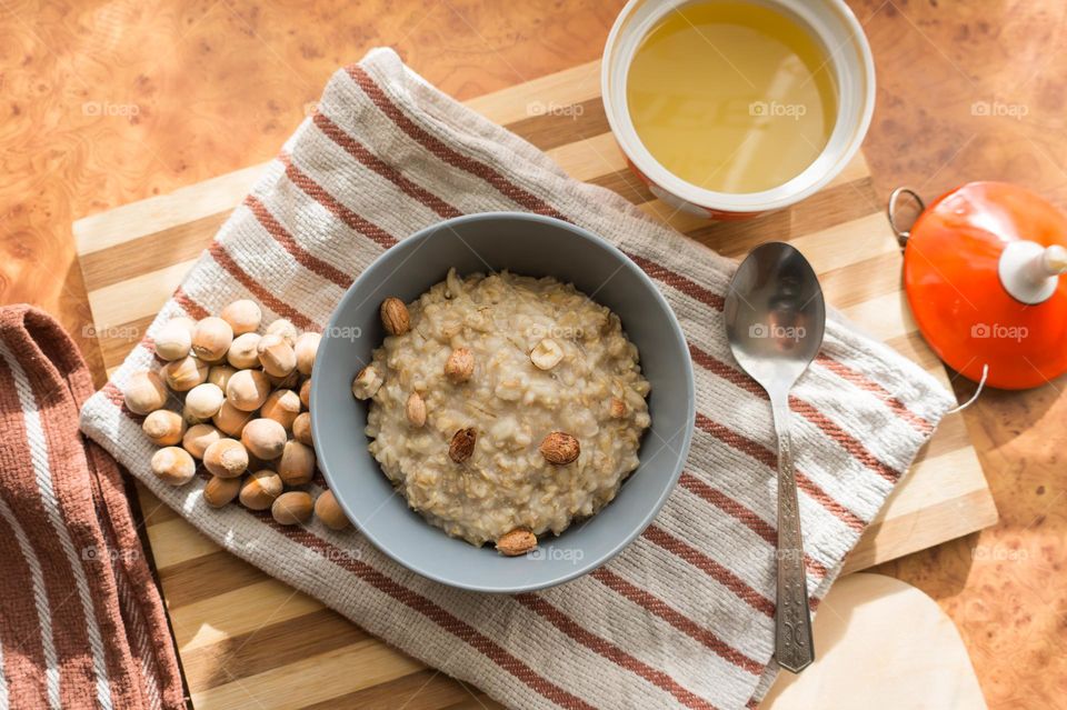 Cooked oatmeal in a deep gray plate with hazelnuts and honey.