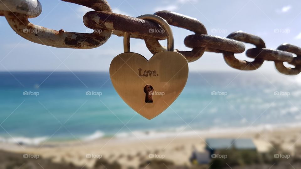 Love, heart shaped padlock hanging on metal chain, by the ocean 