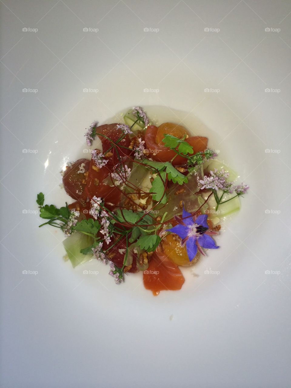 Organic tomato salad, garnished with edible flowers, leafy greens, in shallow white bowl 