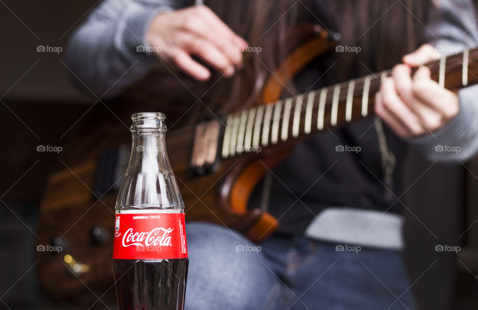 Guitarist woman playing a guitar and Coca Cola drink bottle on foreground