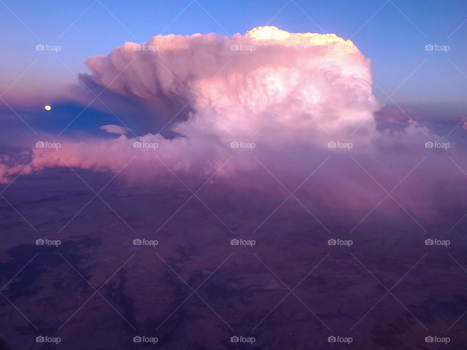 A full moon is visible next to a large cloud at sunset