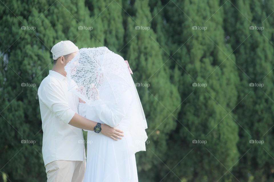 A lovely couple newly bride and groom hug each other wearing white clothes at the garden.