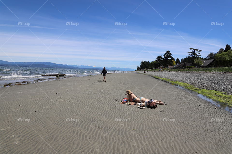 Woman reading while sunbathing on a sandy beach by the ocean 