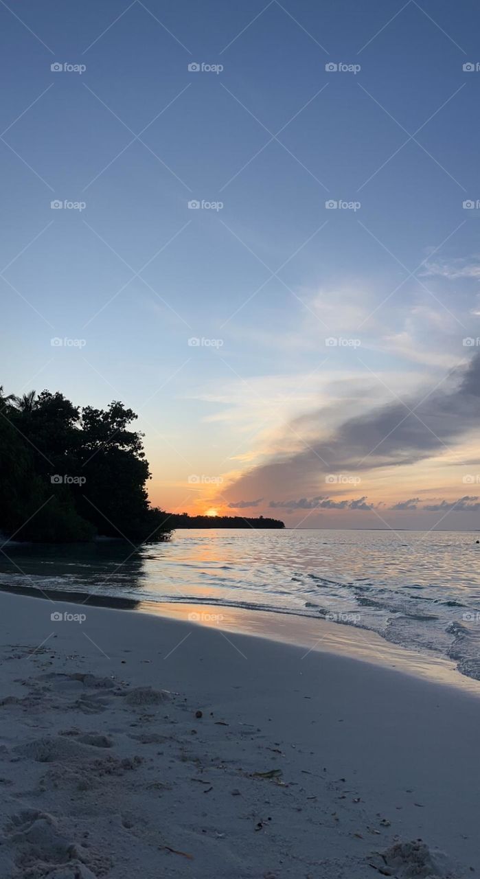Mesmerising scenery of sunrise from behind Thaa atoll Veymandoo island in the Maldives. The sun is slowly approaching with its enchantment while mini-waves crawl on the white sandy beach playing soft music.