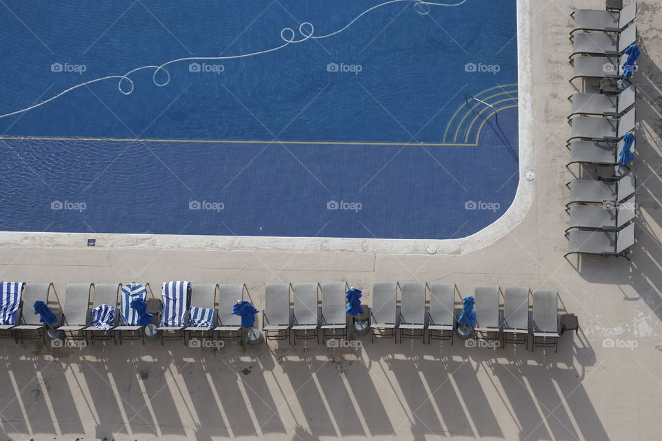 Calm poolside scene with chairs occupied by towels before people arrive.