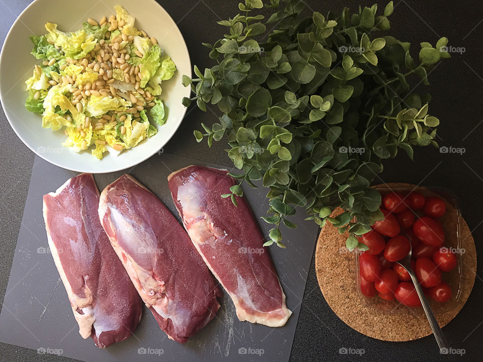 Raw duck fillets with green salad at the table