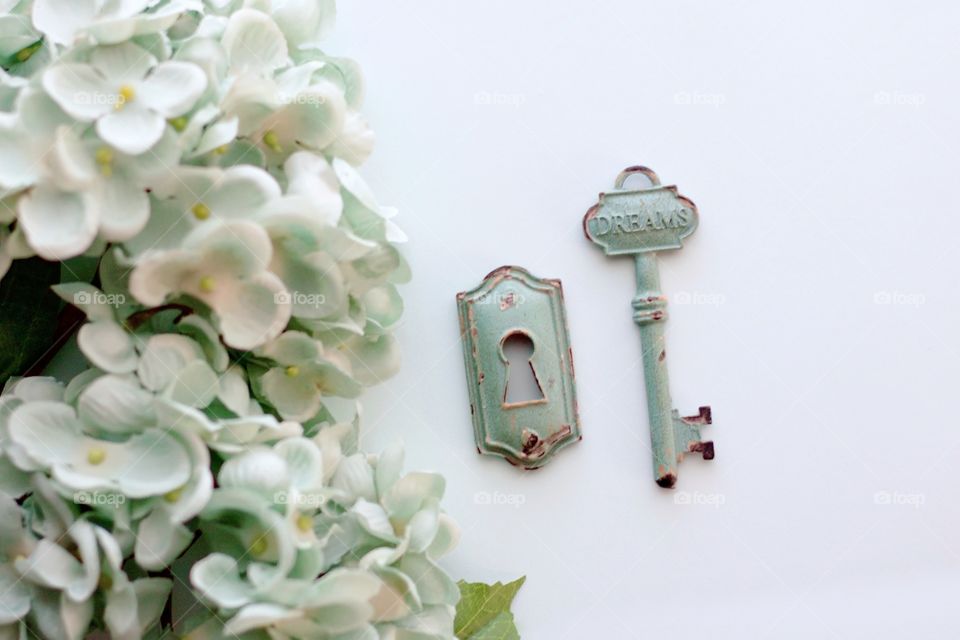 Overhead view of light teal, vintage, metal key with embossed word, “Dreams,” and keyhole with light teal hydrangeas on white background - 