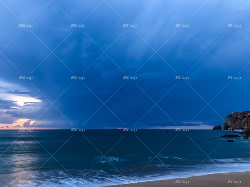 A storm out to sea envelopes the light from the fading sunset as see from the beach at Nazaré, Portugal 