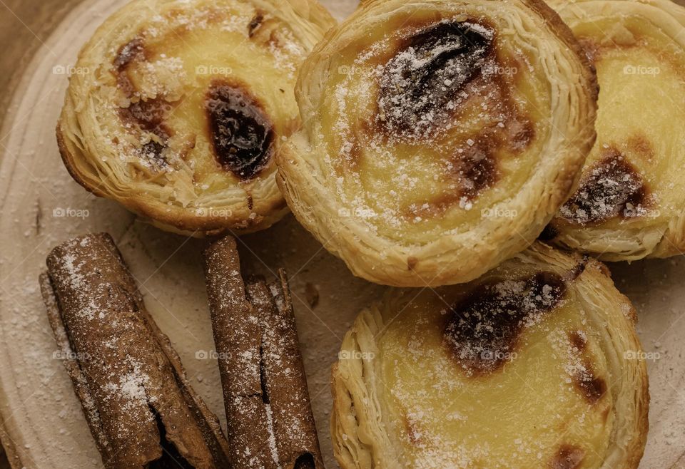 Pastéis de nata served on a wooden platter with cinnamon sticks & sprinkled sugar