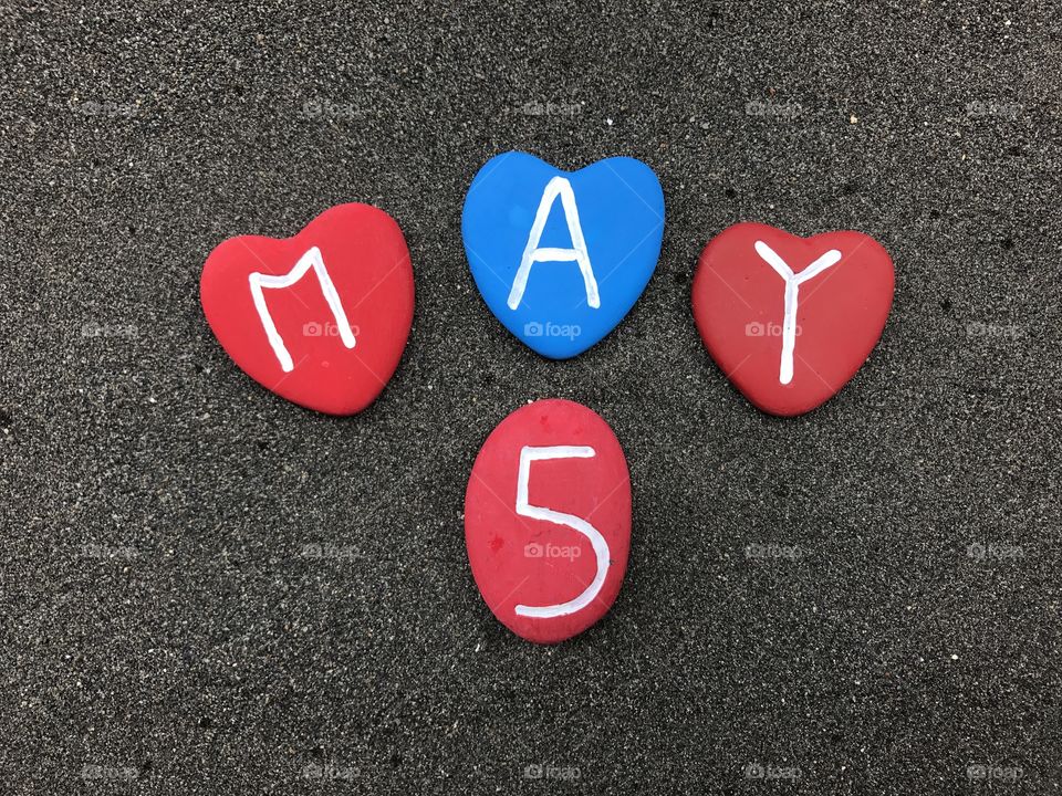 5 May, calendar date with colored stone hearts over black volcanic sand
