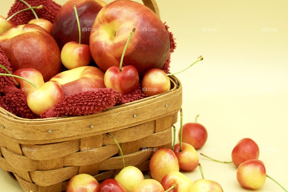 Fruits! - Nectarines And Rainer cherries in a wooden basket against a yellow background 