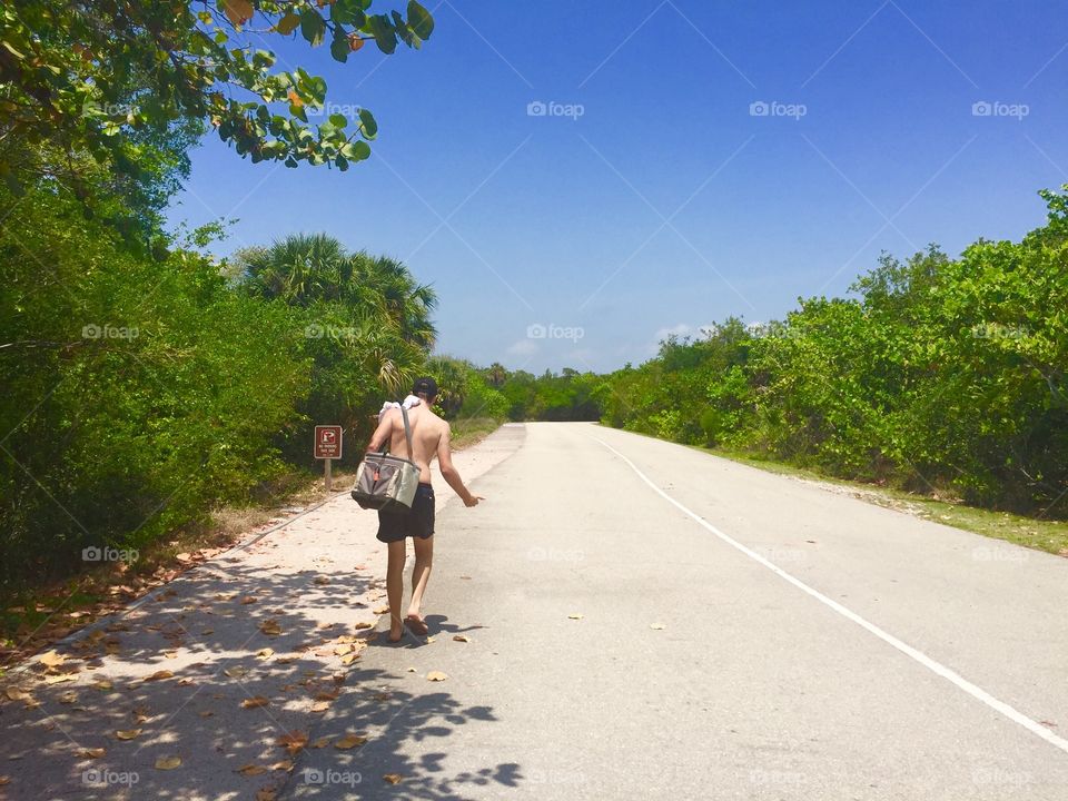 A shirtless walking on the road during summer
