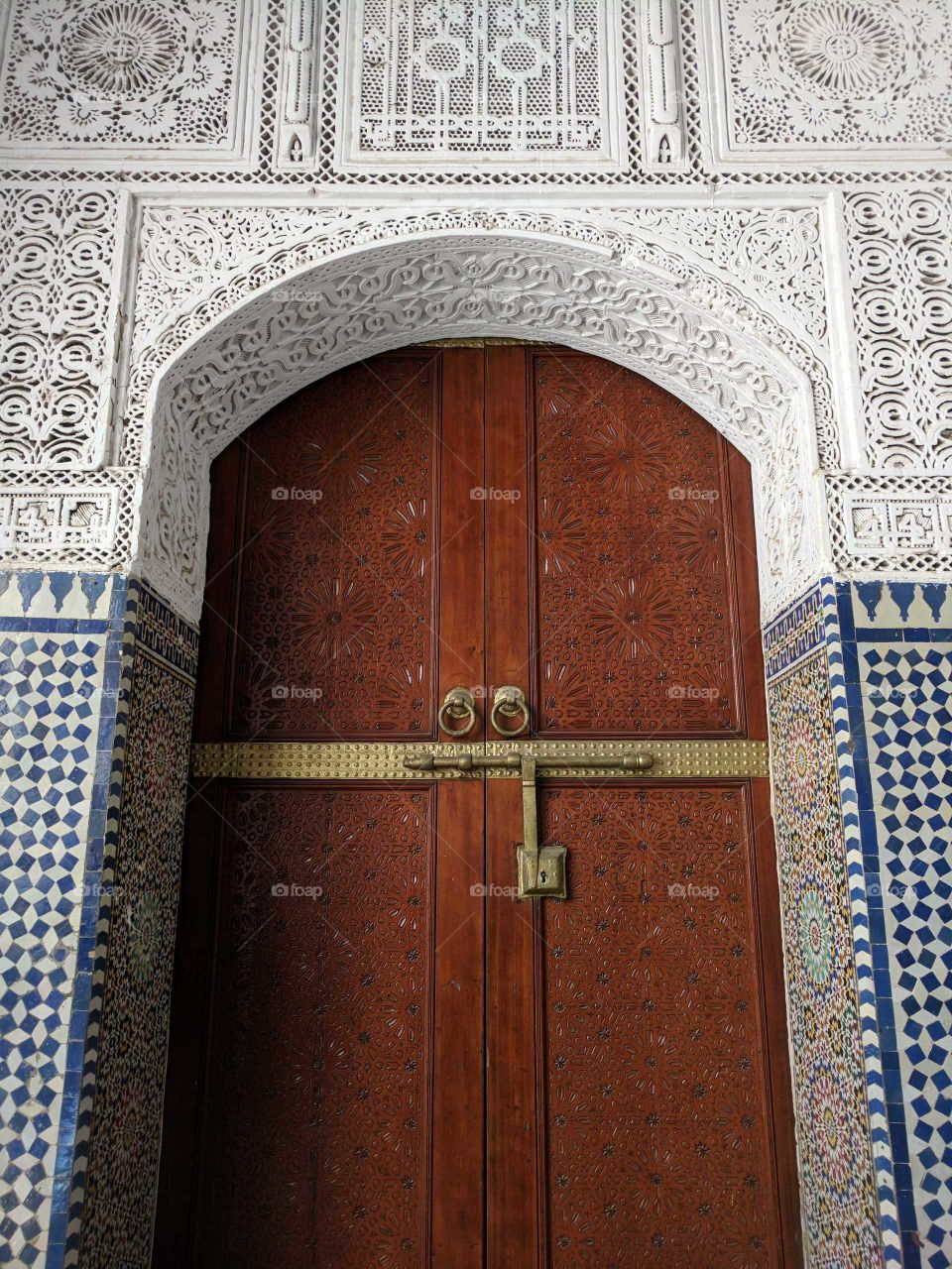 Beautiful, Ornate, Locked Door and Entrance to a House/Mosque/Building in the City of Meknes, Morocco (White Lace and Blue Ceramic Detailing Surrounded a Wood Door Locked with a Gold Lock)