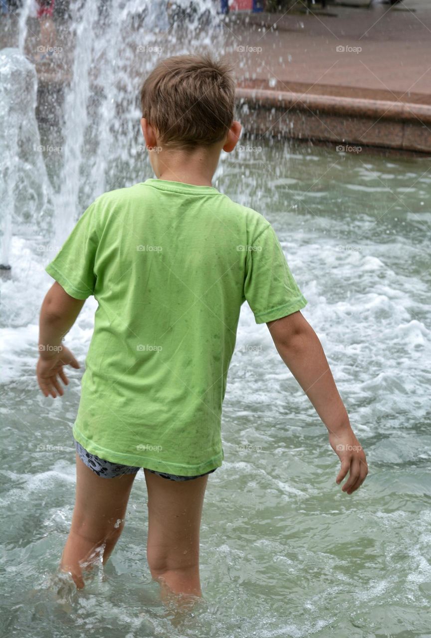 child boy in water fountain urban nature summer time