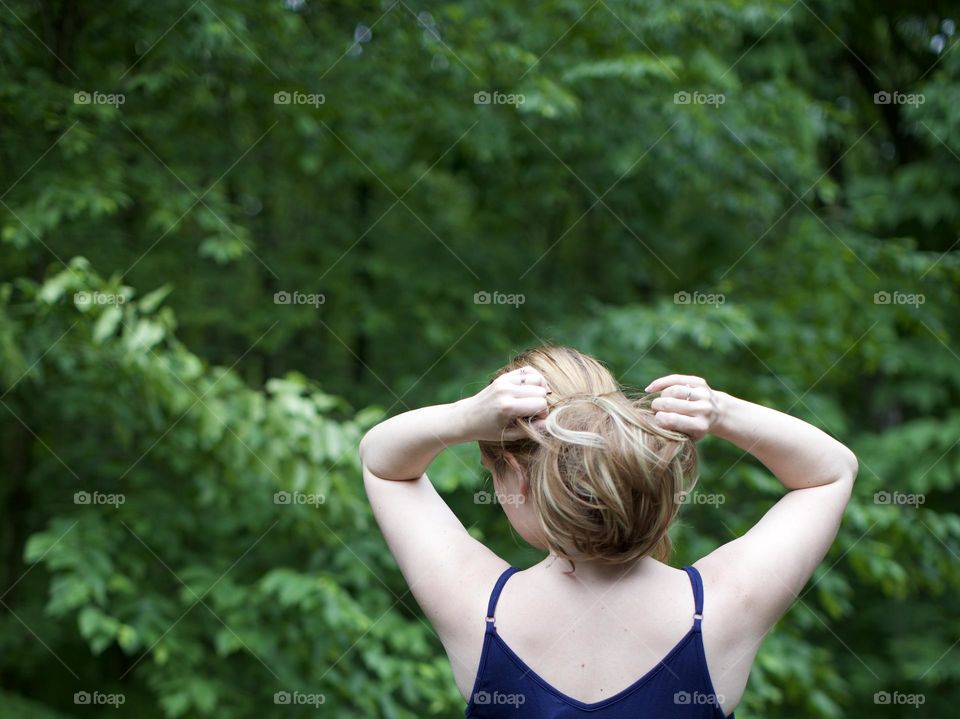 Woman pulling up hair in green,outdoor setting