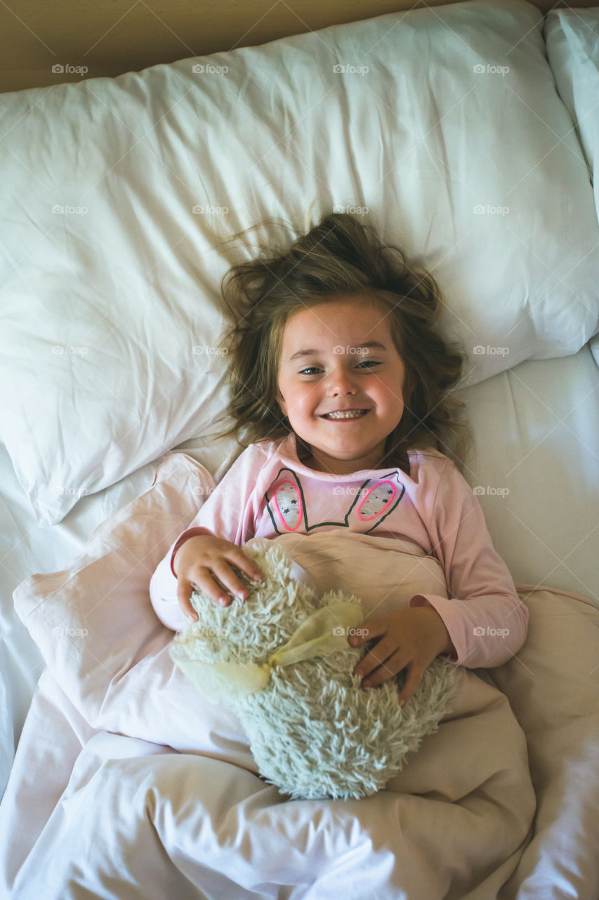 Little girl lying in a bed with teddy bear at the morning