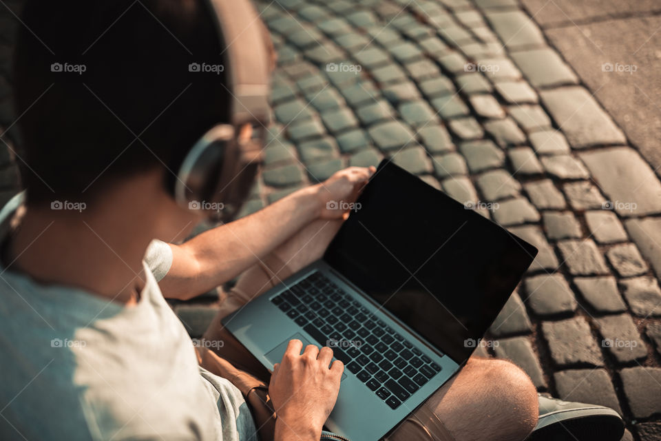 Young man using laptop and wireless headphones outdoor 