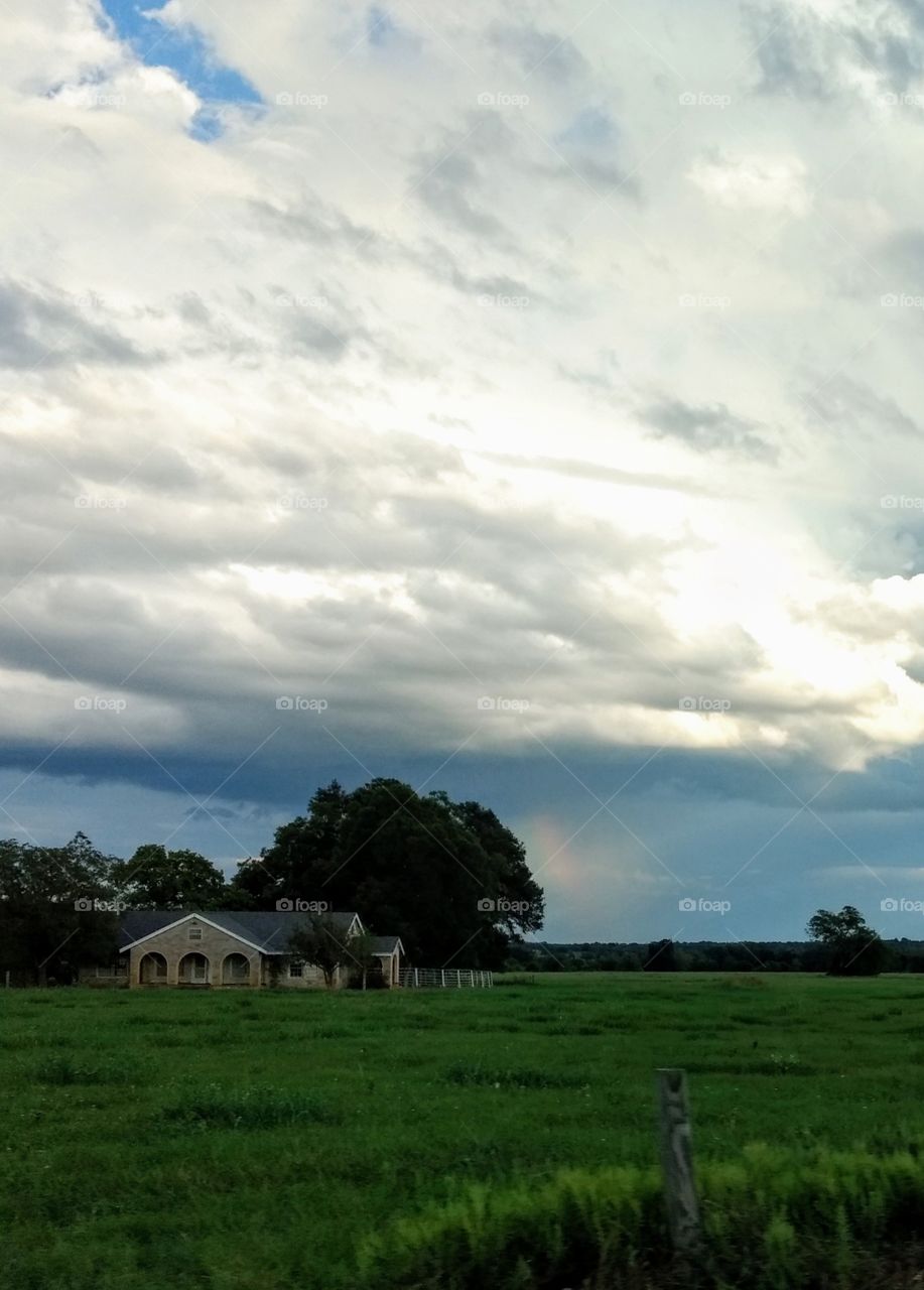 Storm clouds and rainbow over a countryside house home in Texas, clouds, light, rain, landscape, grassy field, farm