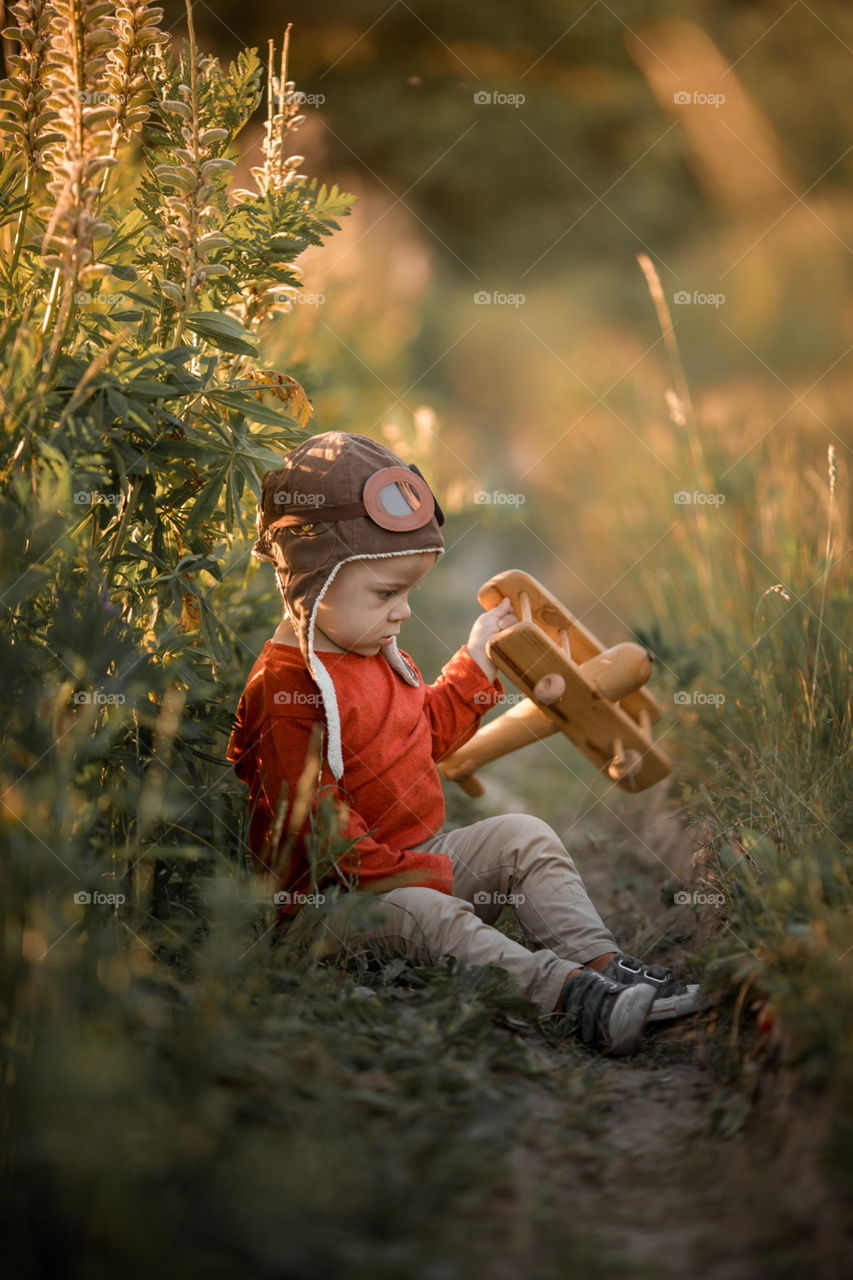 Little boy playing with wooden plane at sunset