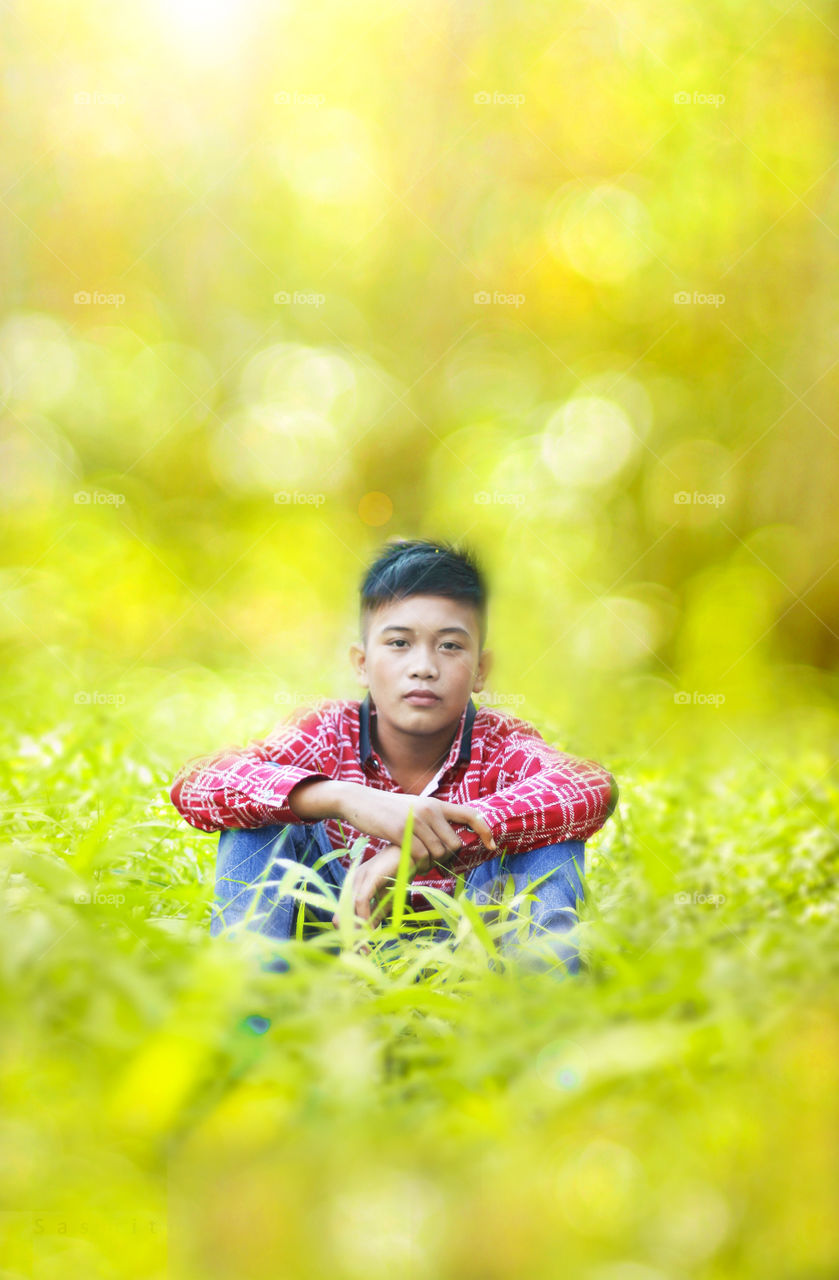 Asian boy sitting in grassy field