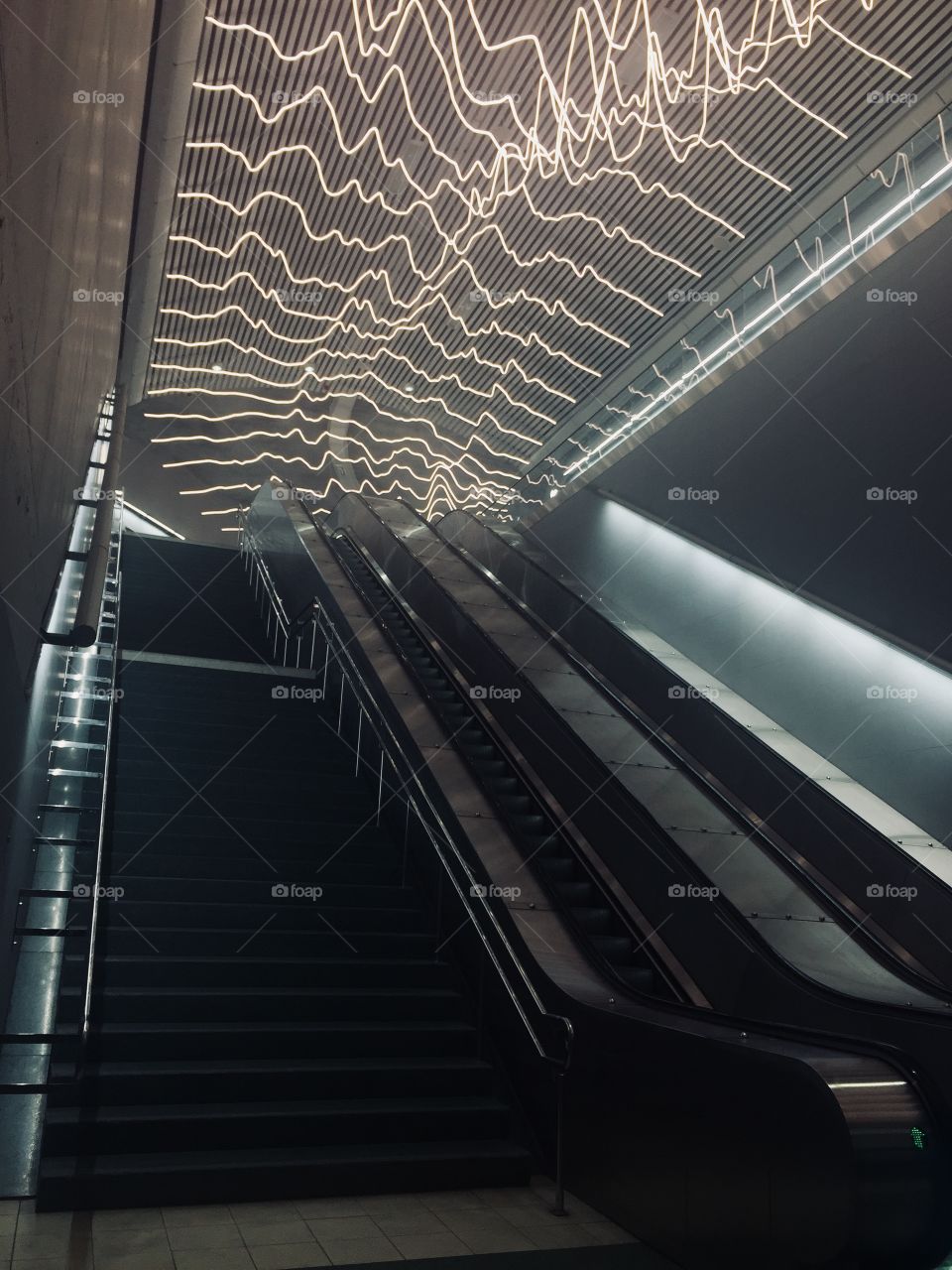 The underground metro station has a unique light installation featuring heartbeat shaped LED lights that cover the ceiling above the tall metal escalators. 