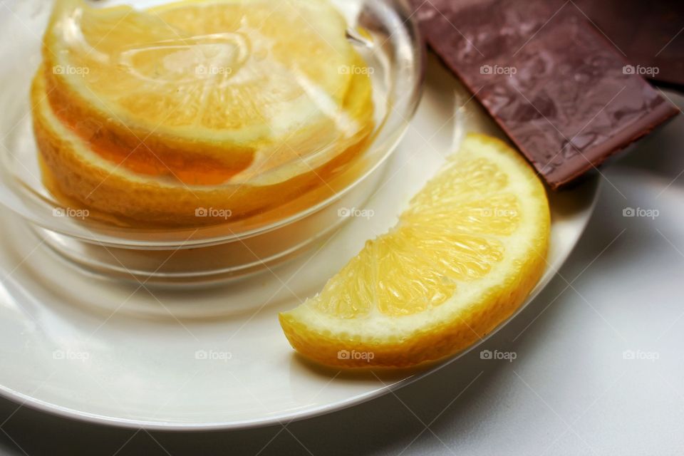 Lemon slices on a white porcelain saucer under a glass cover and cherry chocolate