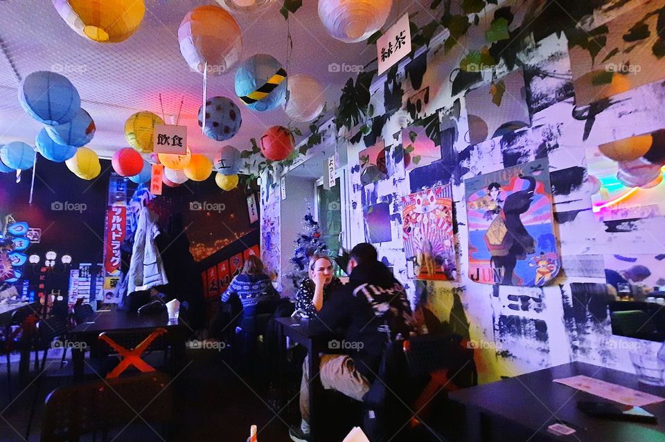 An asian cafe interior design with lanterns and bright pictures on the wall and people at tables