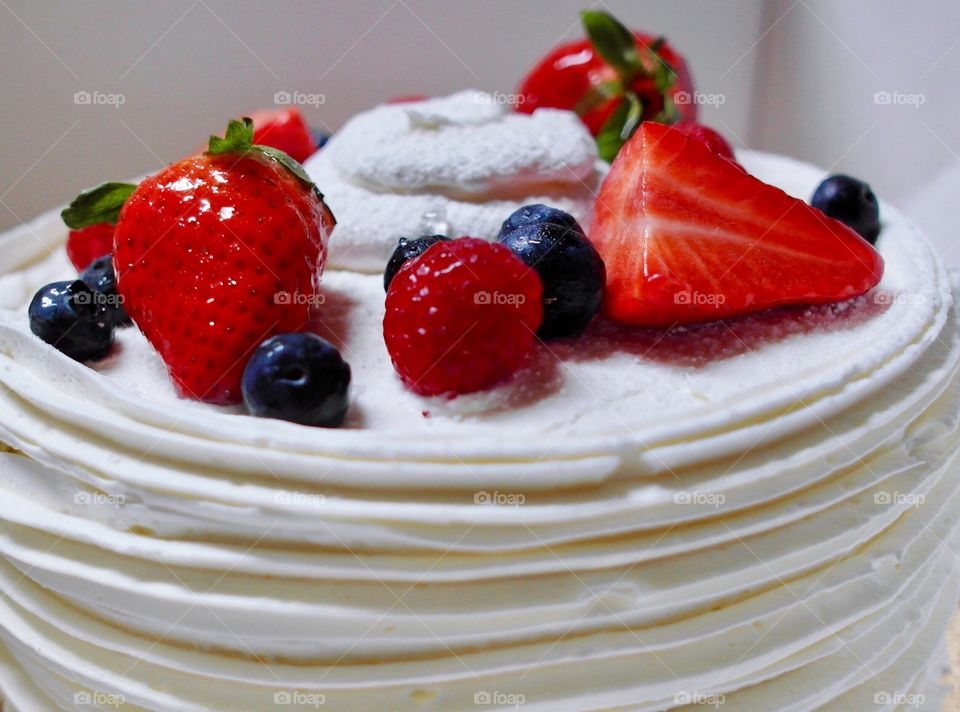 Strawberry, blueberry, raspberry, glazed fruit on top of a white frosted cake
