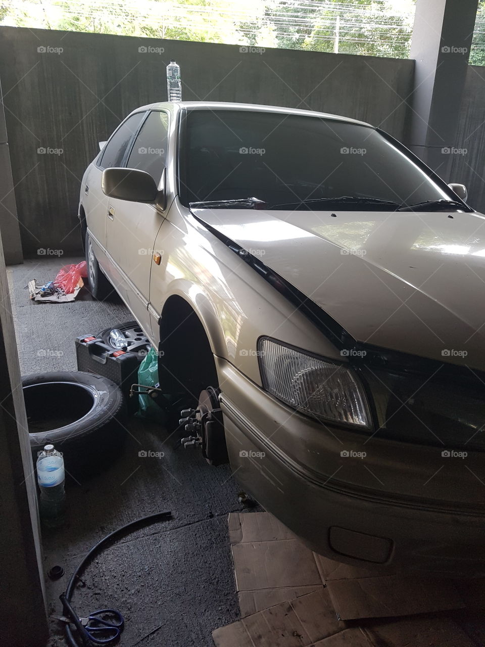 Broken car with missing wheel under repair in a dusty garage