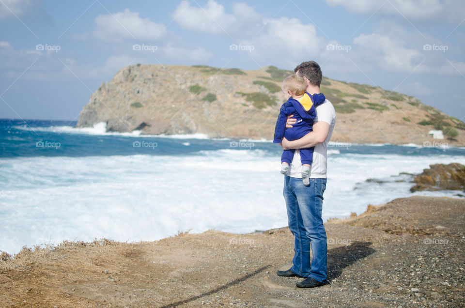 Man standing at coastline and holding his kid