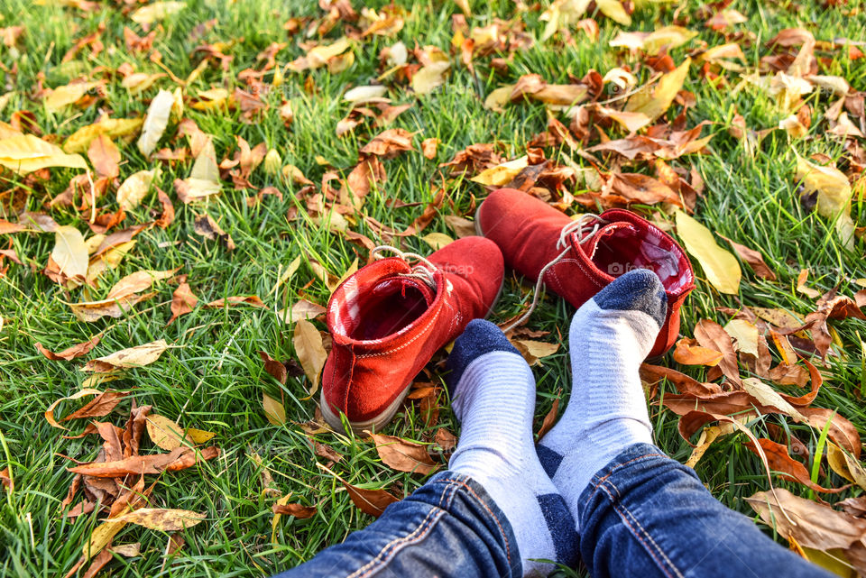 View of person's leg sitting in grass with autumn leaves