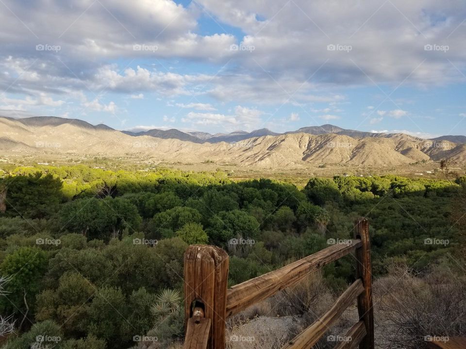 Overlooking a valley of green and distant barren hills. Clouds create shadows.