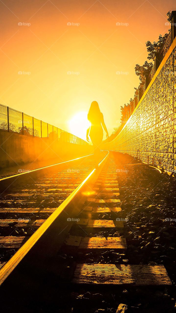 Woman is walking on a railway in the golden light of a sunset