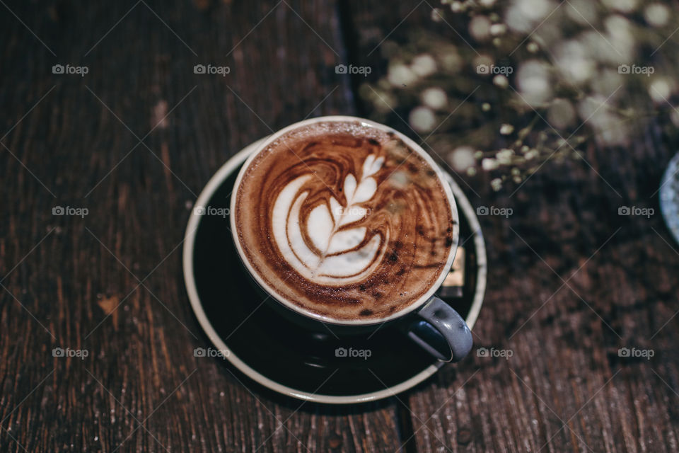 Hot coffee latte on wooden table near white flower