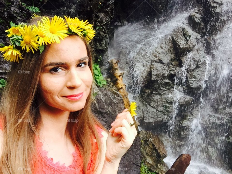 Portrait of woman with flower crown made of yellow flowers and waterfall in the background 