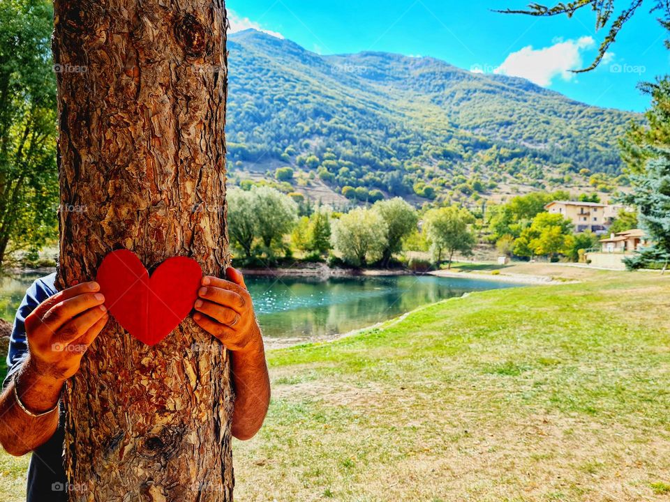 hands hold a red heart placed on the trunk of a tree to express love for nature