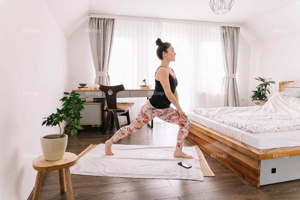 Millennial woman dressed in a black tank top and colorful leggins, doing yoa at home.