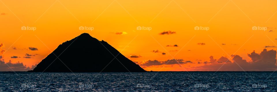 A beautiful orange sunrise behind Moku Nui Islet (Of The Mokes). Kailua, Oahu, Hawaii, USA. 