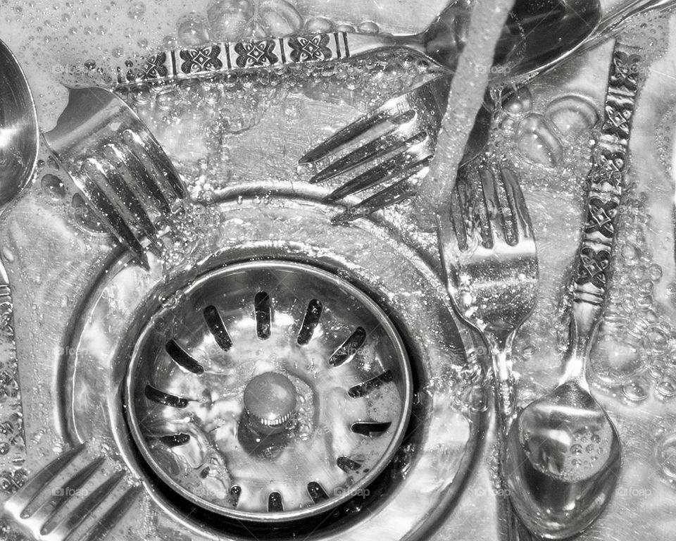 Silverware in a stainless steel sink with running water