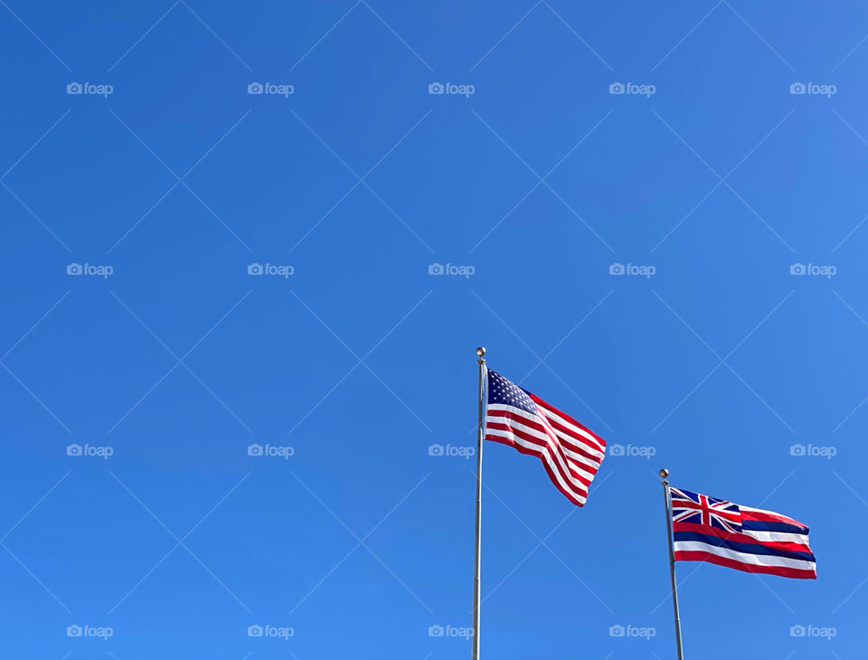 The United States flag and the Hawaii state flag flying side-by-side against a cloudless blue sky 