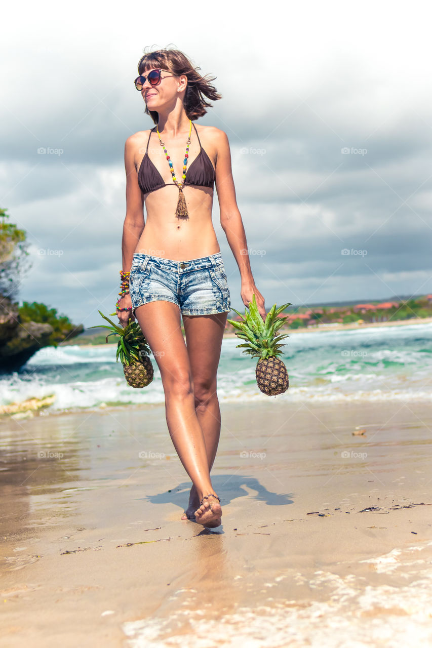 A girl walks along the beach and holds pineapples in her hands. Bali island.